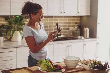 A woman standing in the kitchen chats in a chat before preparing a saladの写真素材