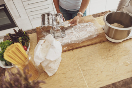 A woman slices noodles on a noodle slicer standing on a table next to a dough mixerの写真素材