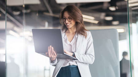 Smiling businesswoman at office with group of colleagues on background, working on laptop