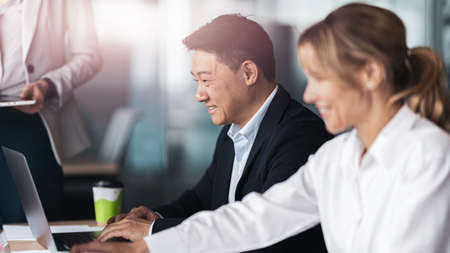 Smiling Business people in meeting room discuss project using laptop