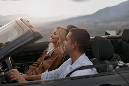 Cheerful young couple man and woman in cabriolet car holding hands feeling happy