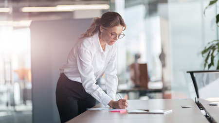 Female lady boss signs documents standing in her workplace at modern officeの写真素材