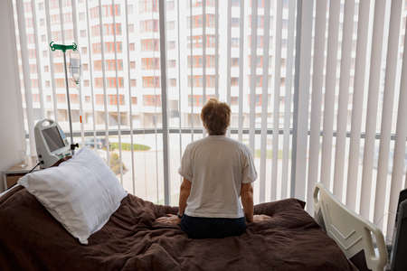 Patient sitting in hospital ward in clinic during the course of treatment and looking window