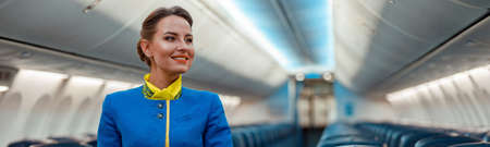 Joyful flight attendant standing in aircraft passenger cabinの写真素材