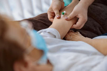 Nurse putting a drip in the arm of her patient in modern medical clinicの写真素材