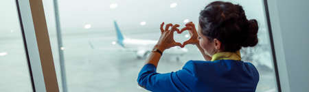 Woman stewardess doing heart symbol in airport terminalの写真素材
