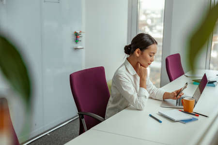 Focused asian business woman sitting in meeting room before conference and holding phoneの写真素材