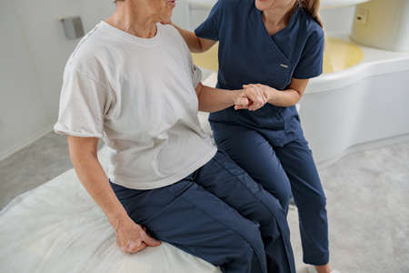 Close up of doctor radiologist help patient sit after procedure of MRI or CT or PET Scan in clinic