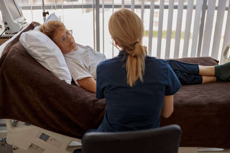 Doctor holding a sick patient by hand supporting her sitting in a hospital room
