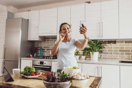 A housewife takes a selfie on her phone camera while preparing a saladの写真素材