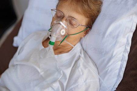 Senior female patient in a breathing mask lies in the ward during treatment for Covid-19の写真素材