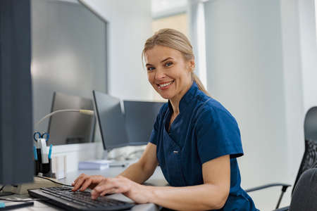 Nurse on Duty working on computer at the Reception Desk in modern clinic and looking cameraの写真素材