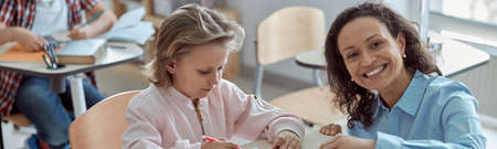 Happy kind teacher is helping kids in elementary school lessons