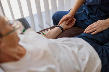 Doctor holding a sick patient by hand supporting her sitting in a hospital roomの写真素材