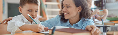 Happy kind teacher is helping a boy in elementary school lessons