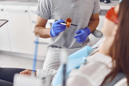 Professional male doctor uses ultraviolet lamp after making a filling on a tooth for joyful happy caucasian woman in modern dental cabinetの写真素材