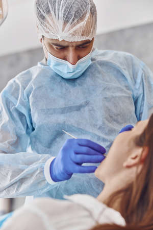 Professional doctor is doing tooth surgery to happy caucasian woman in modern dental cabinetの写真素材