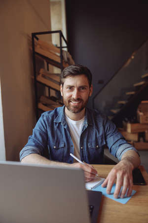 Portrait of handsome Caucasian man sitting in cafe at laptop with pen and notebook and smiling.の写真素材