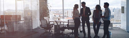 Business team standing against panoramic windows in modern officeの写真素材