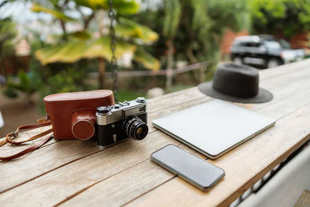 Laptop, hat, phone and photo camera on wooden table