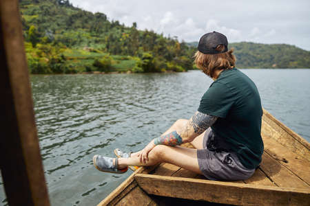 Male tourist sitting on the edge of the boat and looking at natureの写真素材