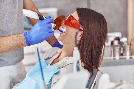 Professional male doctor uses ultraviolet lamp after making a filling on a tooth for joyful happy...