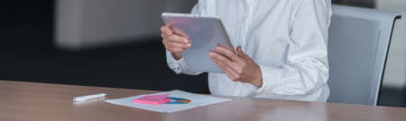 Smiling businesswoman with glasses working on digital tablet at her workplace in office