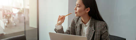 Thoughtful woman looking window while working on laptop in modern office