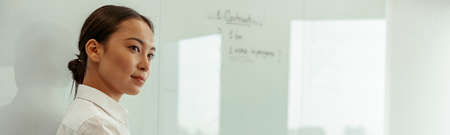 Portrait of asian business woman on background of project planning flipboard looks away