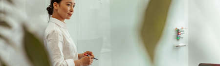 Portrait of asian business woman on background of project planning flipboard looks awayの写真素材