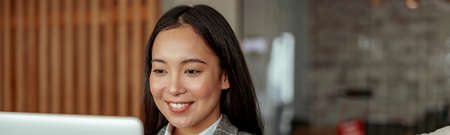 Close up of smiling asian business woman working laptop sitting in cozy office