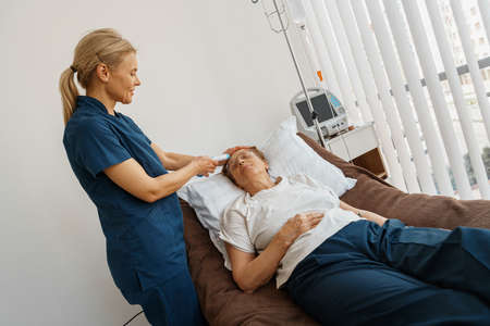 Doctor measures patients temperature with non-contact thermometer in hospital ward