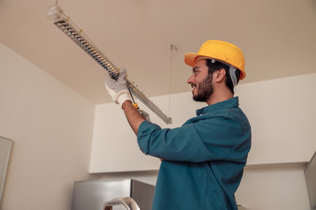 Smiling Professional electrician worker in uniform is installing electric lamps light in kitchenの写真素材