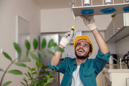 Professional electrician worker in uniform is installing electric lamps light in kitchenの写真素材