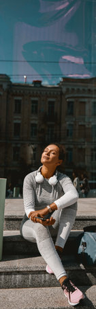 Relaxed sporty woman sitting on stairs while resting after morning workoutの写真素材