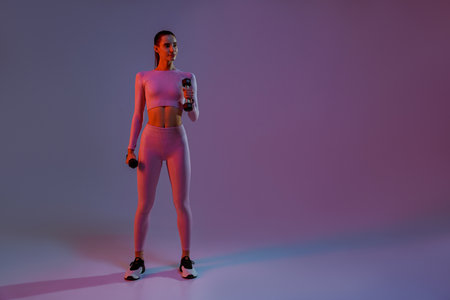 Attractive fitness woman doing exercises with dumbbells on studio background with colored filterの写真素材