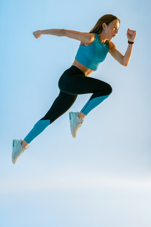 Determined sporty woman running in Mid-Air exercising during cardio workout over studio backgroundの写真素材