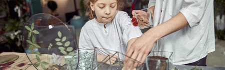 caucasian confident happy florist is working with her young daughter and making composition from glass stones and plants in botanic shopの写真素材