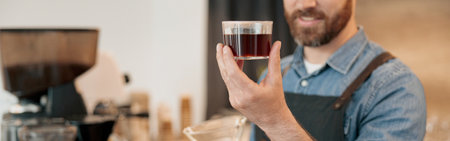 Close up of smiling barista appraisingly looks at a glass of filter coffeeの写真素材