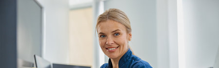 Nurse on Duty working on computer at the Reception Desk in modern clinic and looking camera