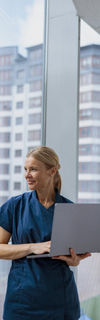 Female healthcare worker using laptop while working at doctors office and looking window