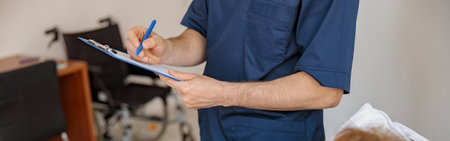 Close up of doctor in mask writing down patient symptoms in hospital ward during Covid-19 epidemic