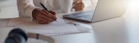 Close up of business woman working laptop and making notes while sitting in modern office