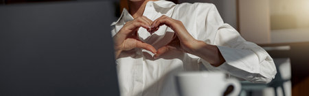 Close up of businesswoman making video call to friends and showing sign love sitting in office