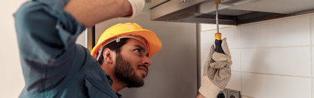 Handyman in uniform repairing kitchen extractor, replacing filter in cooker hood.Maintenance conceptの写真素材