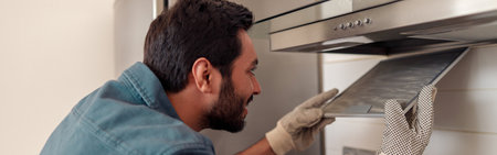 Handyman in uniform repairing kitchen extractor, replacing filter in cooker hood.Maintenance conceptの写真素材