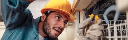 Close up of handyman in special clothing repairing dishwasher in modern kitchenの写真素材