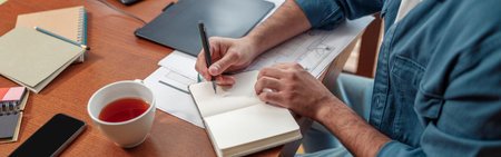 Close up of man hands making notes in notepad while sitting on his workplace