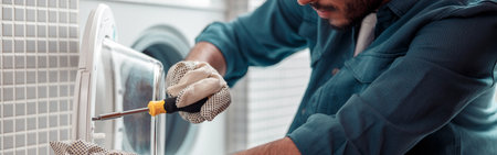 Focused repairman in worker suit is fixing washing machine in bathroomの写真素材