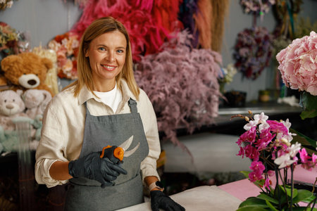 Florist composing bouquet while standing near workplace with tools in flower shop